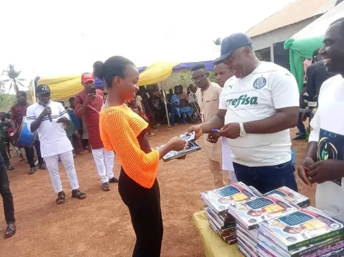 A young woman receives a book from a man in a white shirt, with stacks of books on the table